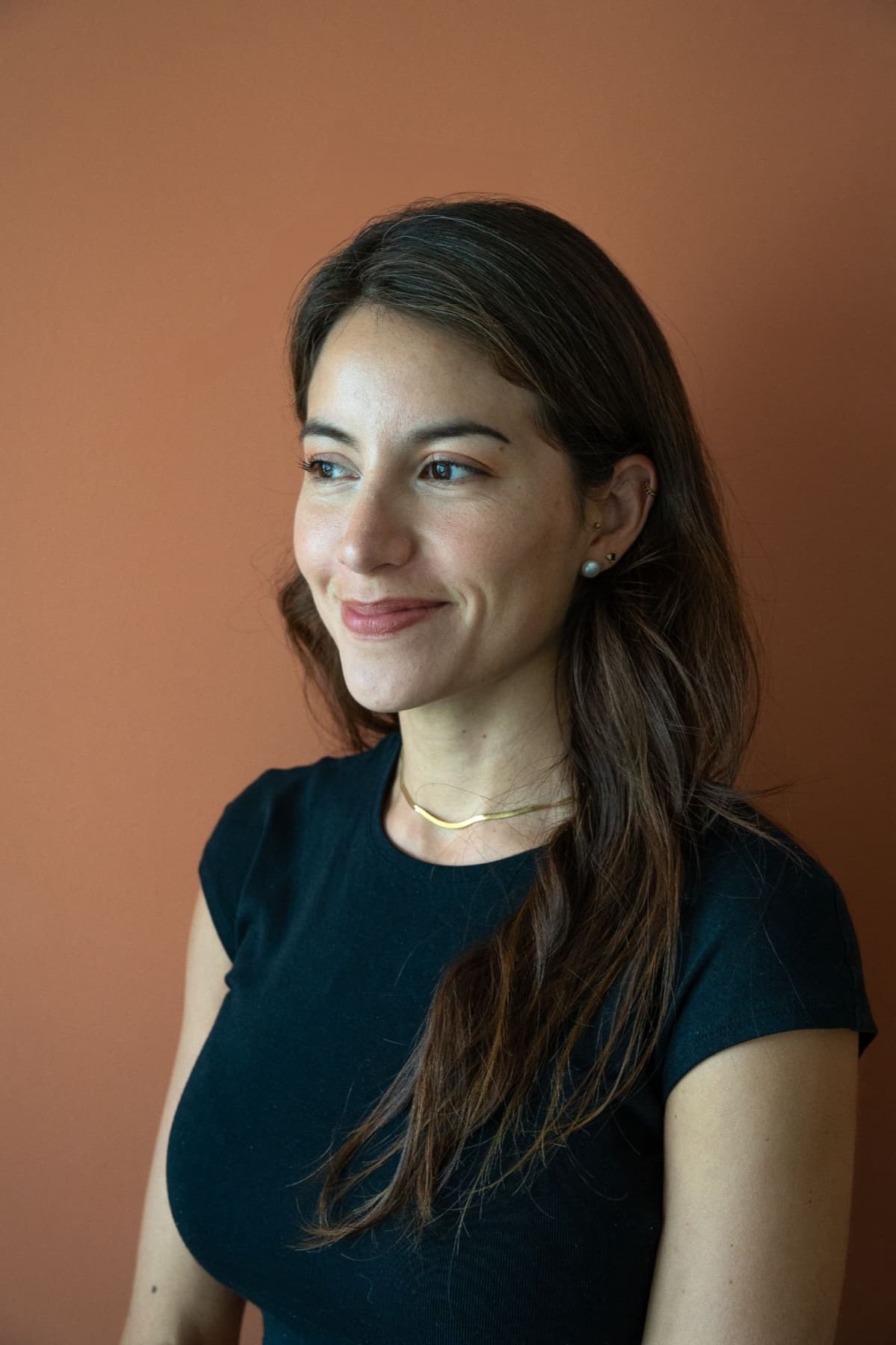 Portrait of Elisa smiling in front of a terracotta wall.